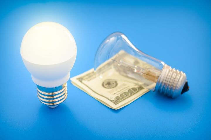 Two light bulbs, one LED and one traditional, on a dollar bill.
