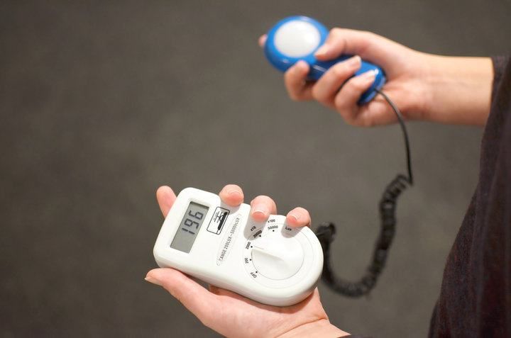 Person holding a light meter and a blue light sensor, measuring illumination.