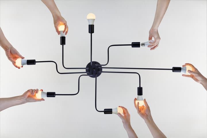 Multiple hands interacting with various LED light bulbs connected to a central fixture.