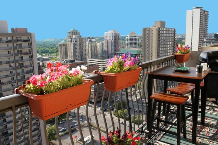 A balcony with flower pots, a table, and a city skyline view.