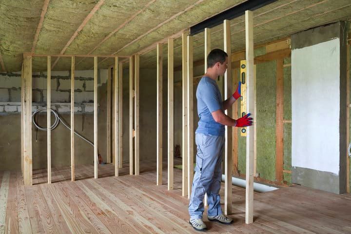 A person uses a level to check wooden framing in a home under construction.