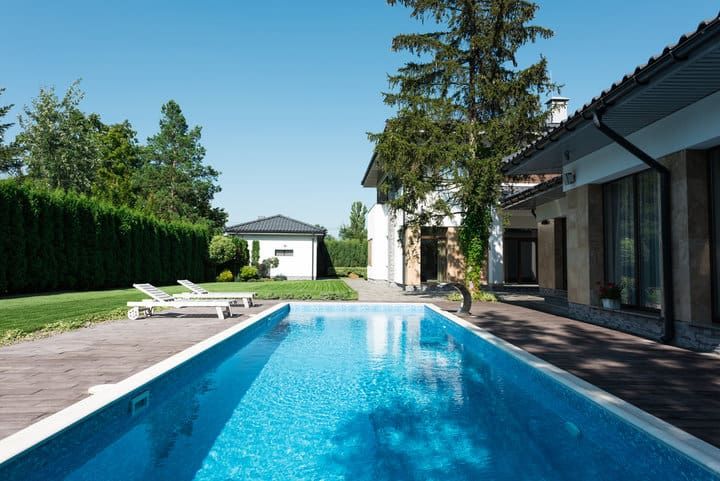A clear blue swimming pool surrounded by green trees and modern houses.
