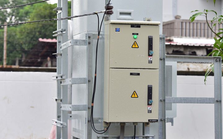 Control boxes with indicators and electrical warnings mounted outdoors near utility poles.