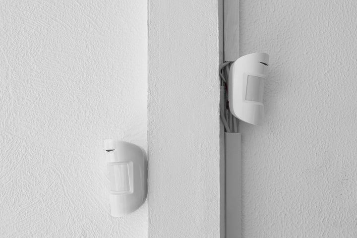 Two white LED motion sensors mounted on a textured white wall.