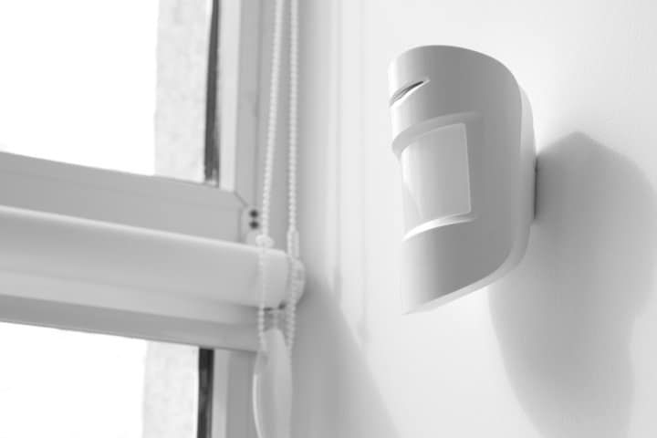 A sleek white motion detector mounted on a wall near a window.