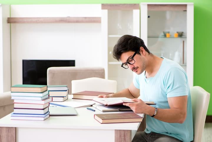 A young man studying at a desk surrounded by books and notepads.