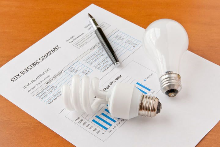 A pen, two light bulbs, and an electric bill on a wooden table.