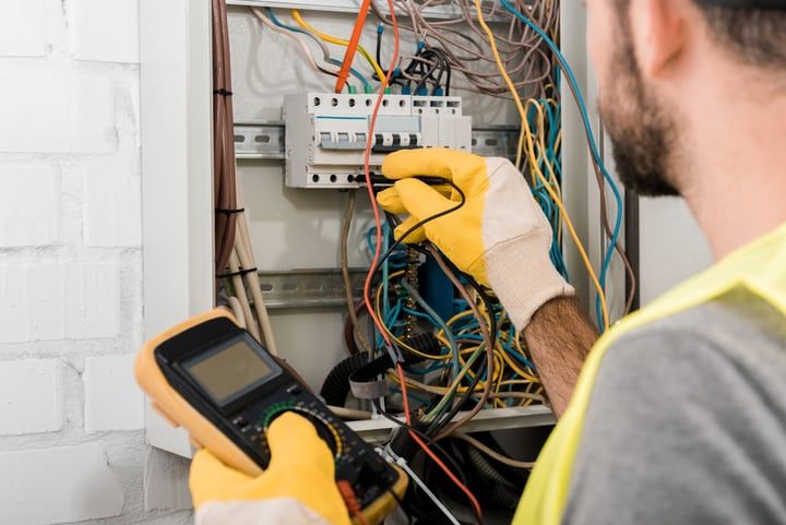 Electrician using a multimeter on a control panel surrounded by colorful wires.