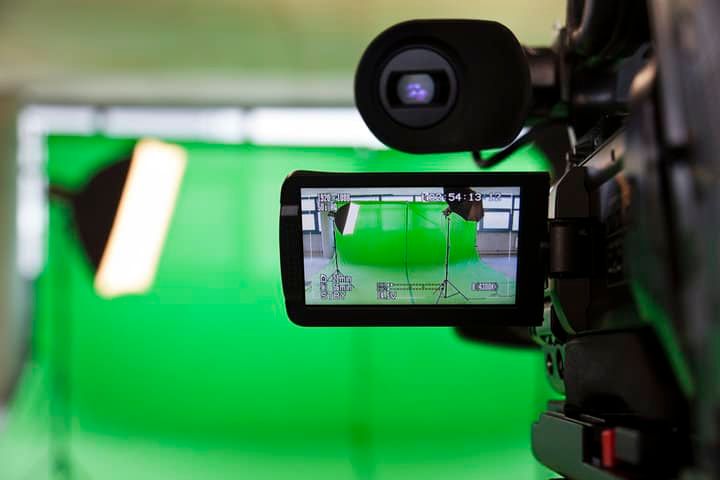 Camera displaying a green backdrop with lighting setup for filming.