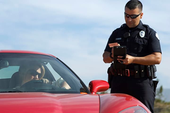 A police officer issues a ticket to a driver in a red sports car.