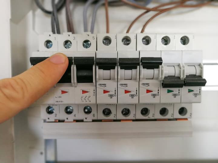 A hand pressing a switch on a row of circuit breakers.