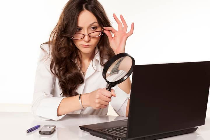 A woman examines her laptop screen using a magnifying glass.