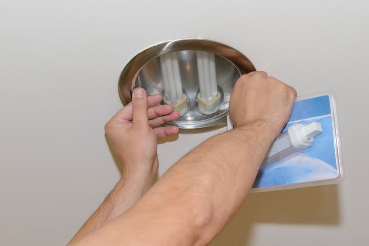 A person replacing a ceiling light bulb with an LED bulb.