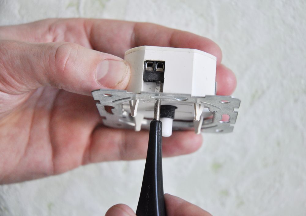 A person holds an LED light fixture with wiring connections visible.