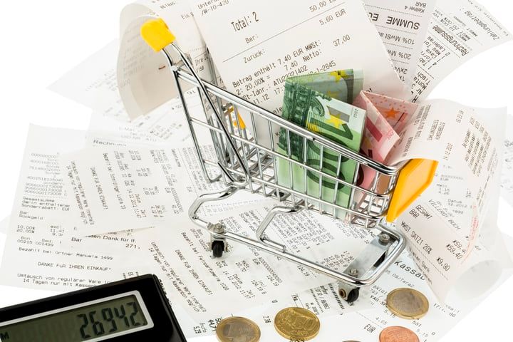 A shopping cart filled with cash and scattered receipts on a table.