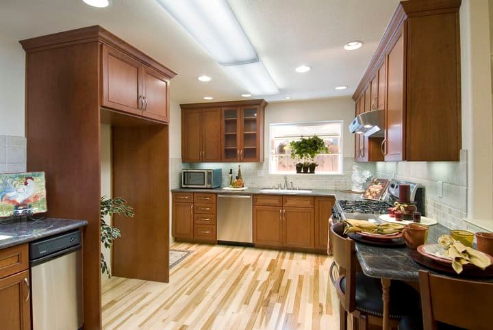 Modern kitchen with LED ceiling lights, wooden cabinets, and bright countertops.