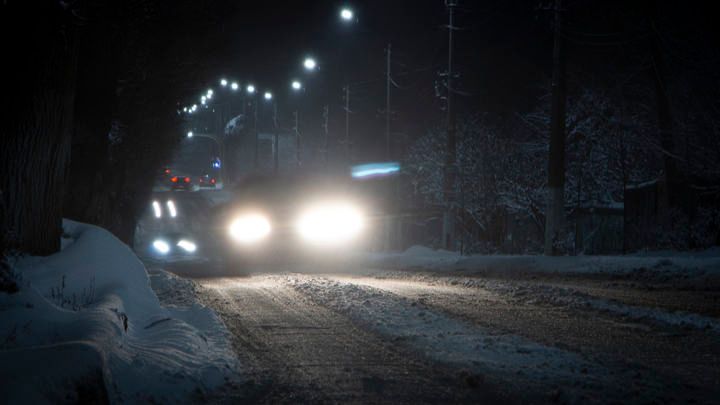Snowy road illuminated by LED streetlights, with headlights of a car approaching.