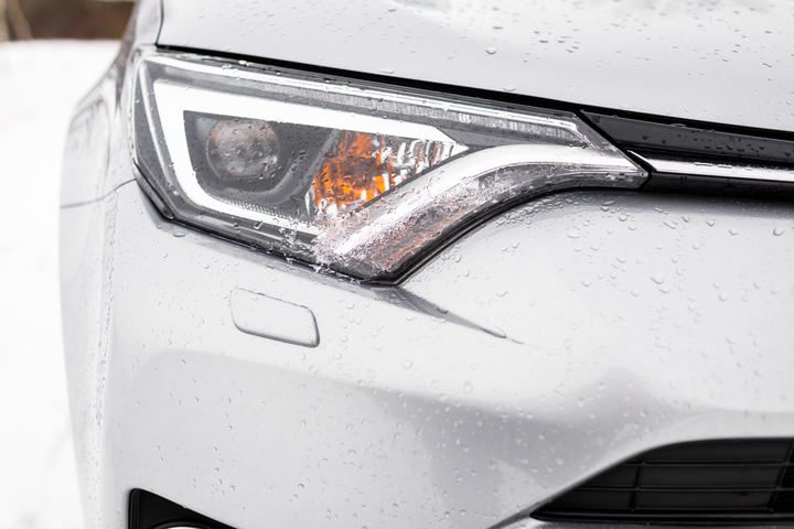 Close-up of a car headlight with raindrops on it, showcasing LED technology.