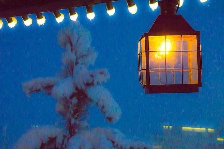 A glowing lantern hangs beside a snow-covered tree against a blue sky.