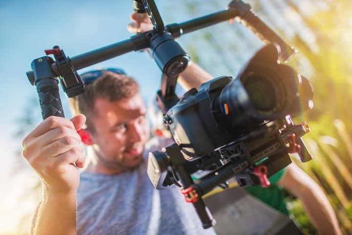 Person using a stabilizer to film with a camera outdoors, sunlight reflecting.