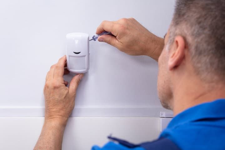 A person installing a motion sensor on a white wall.