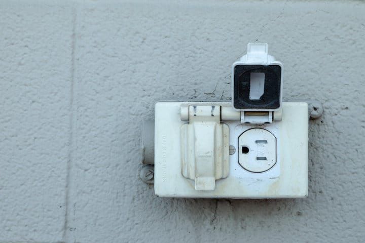 A weathered electrical outlet with a white casing on a gray wall.