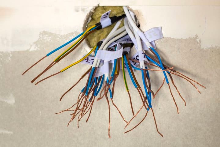 Wiring with multiple color-coded cables emerging from a wall opening.