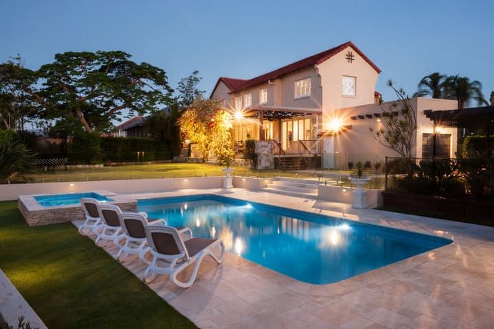 A beautifully lit backyard featuring a pool, lounge chairs, and a modern house.
