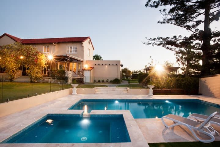 Modern home with illuminated swimming pool and landscaped garden at dusk.