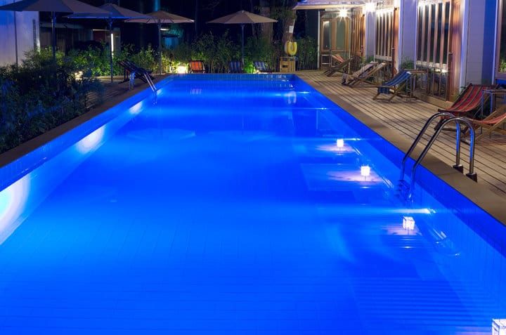 A serene outdoor swimming pool illuminated by blue LED lights at night.