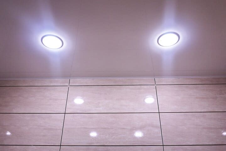 Two round LED ceiling lights illuminate a glossy tiled wall below.
