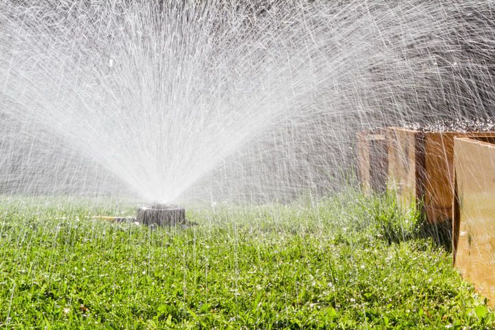 A sprinkler spraying water over a green lawn with wooden boxes nearby.