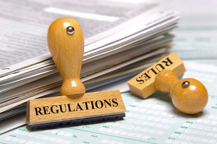 Wooden stamps labeled Regulations and Rules with paperwork in the background.