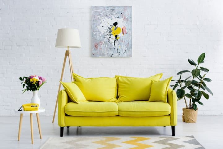 Bright yellow sofa with pillows, lamp, and plants in a modern room.