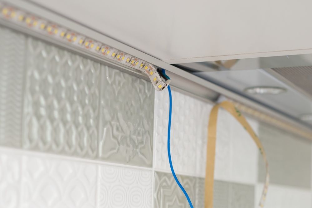 Close-up of LED strip lights attached to a textured kitchen wall.