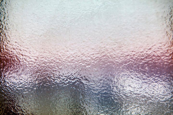 Softly blurred, textured glass surface with subtle color gradients behind.