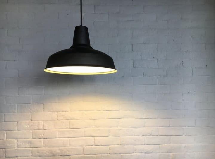 A modern black pendant light hanging above a white brick wall.