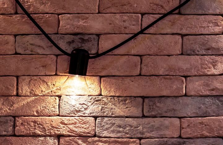 Illuminated vintage light bulb hanging against a textured brick wall.