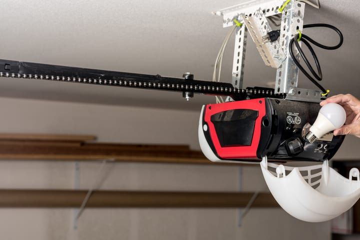 A person installing a light bulb in a garage door opener.