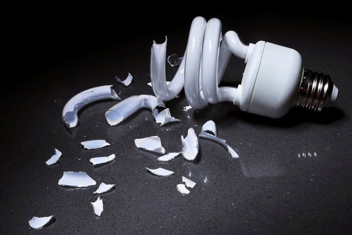 A broken spiral LED bulb lies shattered on a dark surface.