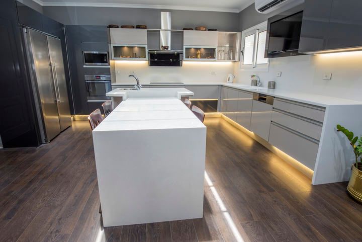 Modern kitchen with sleek cabinets, illuminated countertops, and wooden flooring.