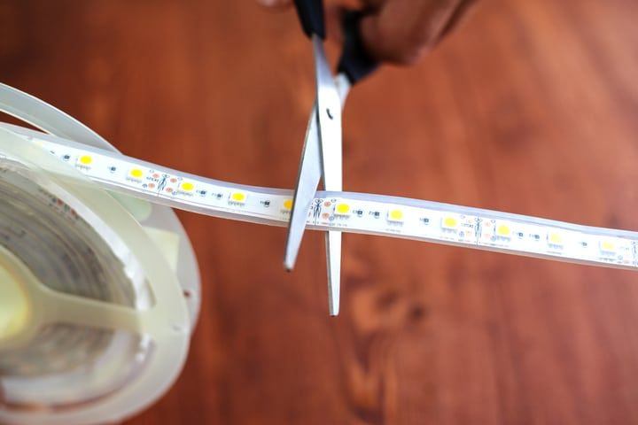 A person cutting LED light strip with scissors on a wooden surface.