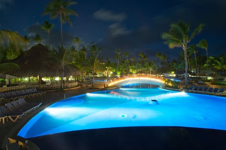 Illuminated pool area at night with palm trees and lounge chairs