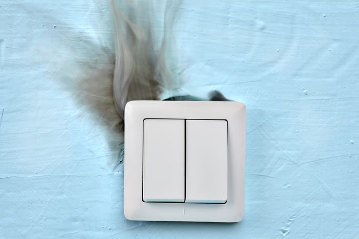 A light switch with smoke and scorch marks behind it on blue wall.