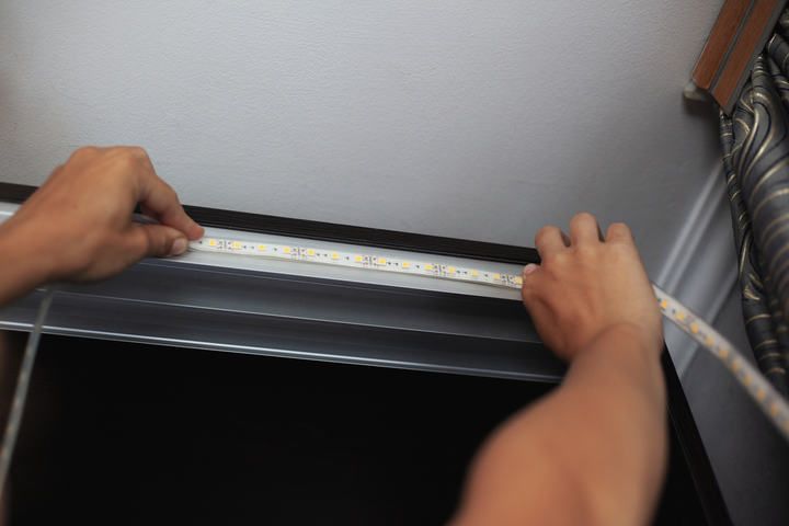 Two hands installing LED strip lights along a ceiling corner.