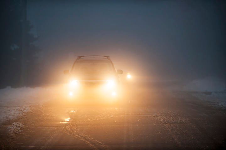 A vehicle with bright headlights driving in foggy winter conditions.
