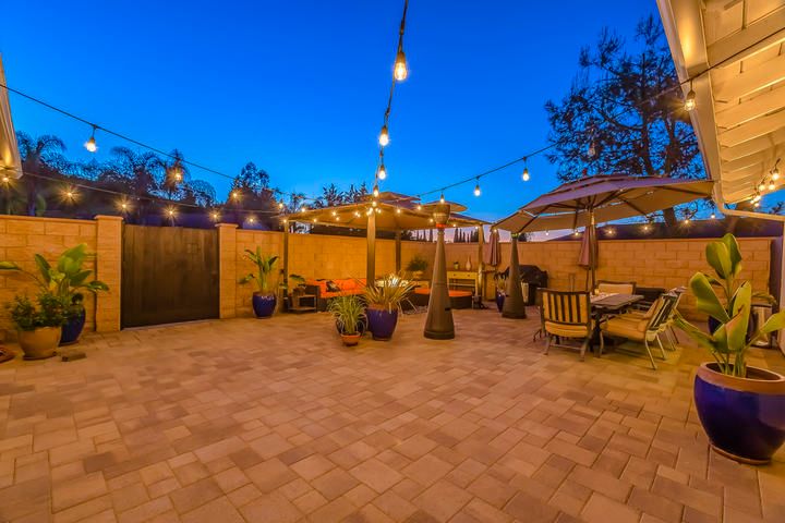 Brightly lit patio with string lights, seating areas, and potted plants at twilight.