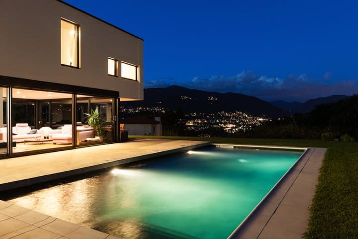 Modern house with a pool illuminated at night overlooking a city skyline.
