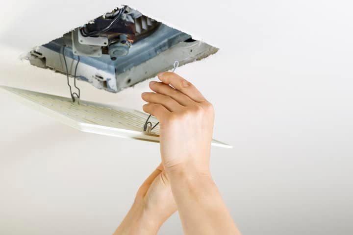 A person installing an LED panel light into a ceiling fixture.