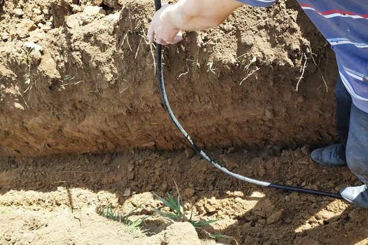 Person working on a trench, laying down black tubing in soil.